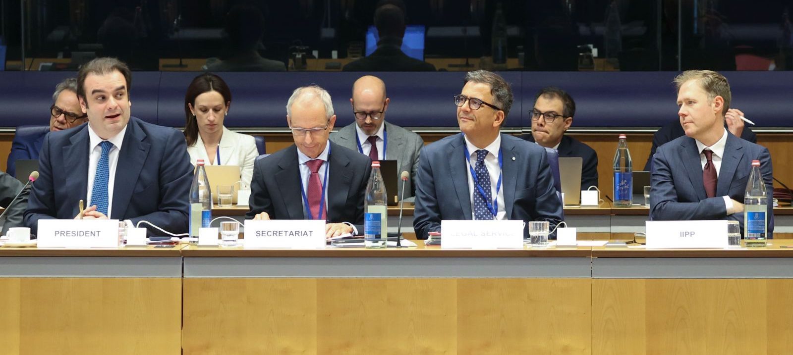 Picture of the head table during the Eurogroup meeting. Kyriakos Pierrakakis is talking on the left hand side, David Eaves is listening on the right hand side, in between them sit two members of the Eurogroup secretariate